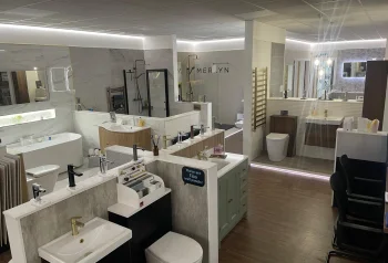 Bright bathroom showroom featuring sinks, taps, toilets, a freestanding tub, marble walls, mirrors and display cabinets.