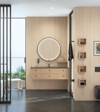 Minimalist interior with light wood walls, floating six-drawer vanity, black countertop, and round backlit mirror; glass divider and outdoor greenery visible.