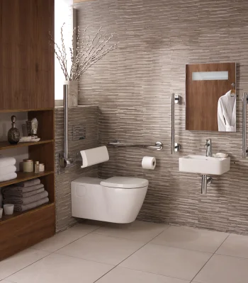 Modern accessible bathroom with wall-mounted toilet and sink, wooden storage shelves, beige mosaic wall tiles, mirror, grab bars and towels.